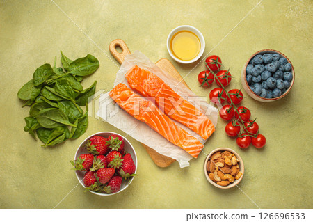 Healthy food for anti inflammatory diet: fish, vegetables, berries, nuts, olive oil, spinach top view on green background 126696533
