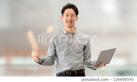 一位微笑的男性商人，手裡拿著電腦，揮拳 126698543