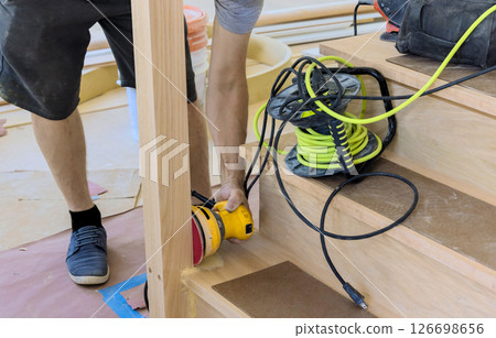 Worker carefully sands wooden stairs, surrounded by tools materials, in residential renovation underway 126698656