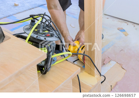 Contractor on using power tool to refine edges of wooden stairs during home improvement project. 126698657