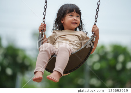 cheerful toddler girl playing on a swing at playground cheerful toddler girl playing on a swing at playground 126698919