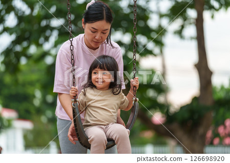 cheerful toddler girl with mother playing on a swing at playground cheerful toddler girl with mother playing on a swing at playground 126698920