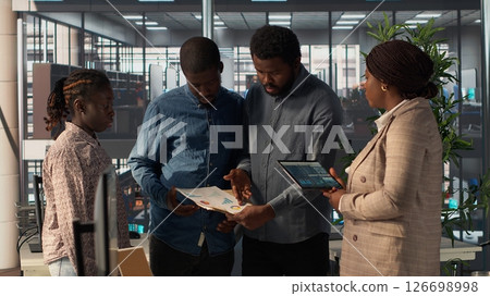 Black leader reviews company strategy with her team members in a modern corporate office, making key business decisions to support organizational growth. Discuss resource allocation. Camera B. 126698998