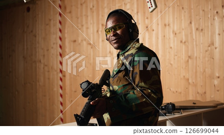 Portrait of happy soldier holding assault rifle, developing marksmanship skills in firing range. Joyous military unit wearing uniform practices with semiautomatic weapon, camera A Portrait of happy soldier holding assault rifle, developing marksmanship skills in firing range. Joyous military unit wearing uniform practices with semiautomatic weapon, camera A 126699044