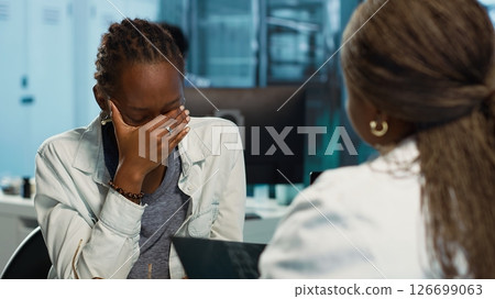 Female physician and patient examining health care reports focusing on cancer diagnosis, radiation therapy and wellbeing strategies to combat illness in a professional clinic setting. Camera A. 126699063