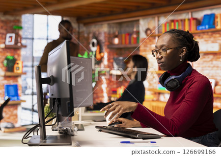 Programmer in startup office using large language model to get help with coding project. African american worker interacting with AI LLM chatbot PC GPT software on PC in software development workplace 126699166