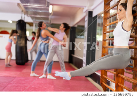 Fit slim young woman training in gym, performing leg raises on wall bars. Bodyweight exercises to strengthen muscles. Fitness concept 126699793