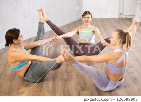 Three young women practicing yoga poses perform a joint exercise Three young women practicing yoga poses perform a joint exercise 126699908