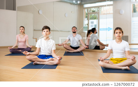 Sporty parents and teenage kids sitting in lotus position in yoga studio Sporty parents and teenage kids sitting in lotus position in yoga studio 126700072