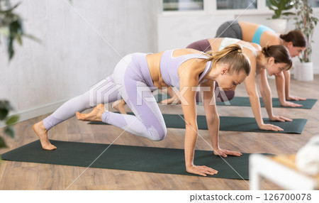 Woman doing knee to elbow plank pose in yoga studio Woman doing knee to elbow plank pose in yoga studio 126700078