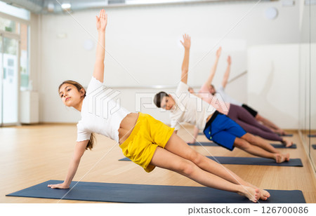 Girl practicing side plank with family in gym 126700086