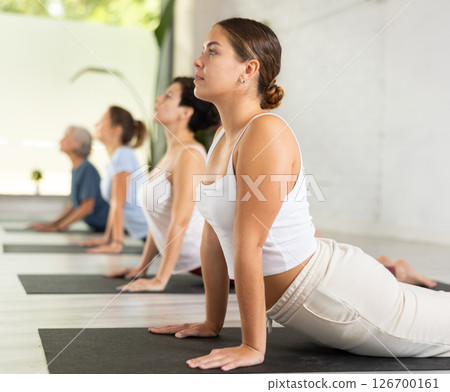Young female doing cobra pose for health care and wellness with group together at yoga studio 126700161