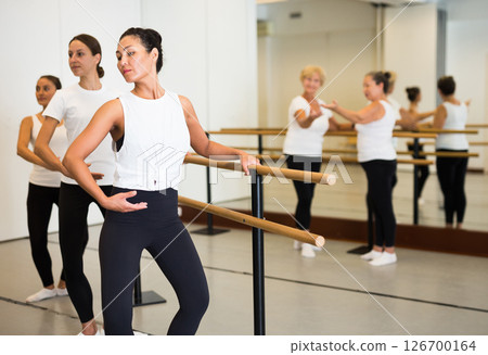 Dancing Asian woman perform demi plie near the ballet barre, standing in a ballet stance 126700164