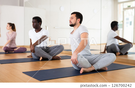 Man practising lotus pose with group in gym 126700242