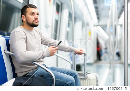 Bearded traveler sitting with suitcase and smartphone in metro car 126700245