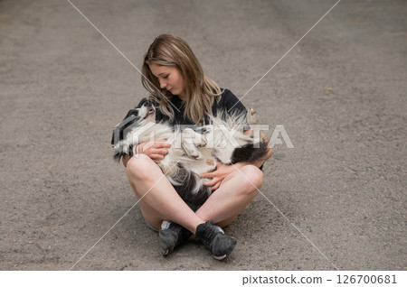 Young caucasian woman sitting on asphalt and hugging border collie dog.  126700681