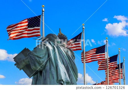 Statue of Liberty stands proudly with multiple American flags fluttering in Ney York US 126701326