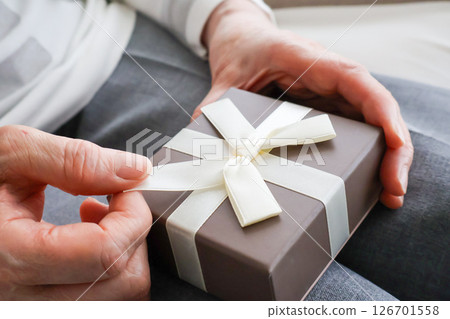 Hands of an elderly woman undoing the ribbon on a gift 126701558