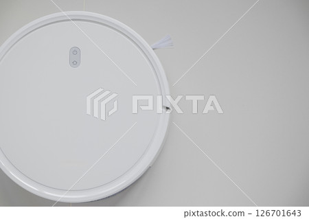 White automatic floor cleaner with side brush on tile flooring. Top view of robot vacuum cleaner removing dust, showcasing modern smart home cleaning technology for spotless and efficient maintenance White automatic floor cleaner with side brush on tile flooring. Top view of robot vacuum cleaner removing dust, showcasing modern smart home cleaning technology for spotless and efficient maintenance 126701643