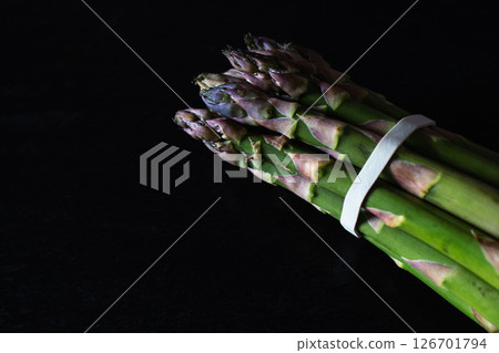 Raw asparagus on black background. Green and violet asparagus on dark stone surface. Springtime vitamins. Healthy eating. Farm to table concept. Asparagus bundle isolated. Raw asparagus on black background. Green and violet asparagus on dark stone surface. Springtime vitamins. Healthy eating. Farm to table concept. Asparagus bundle isolated. 126701794