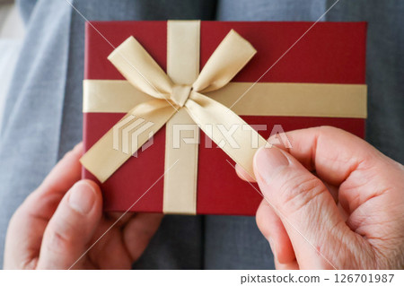 Hands of an elderly woman undoing the ribbon on a gift 126701987