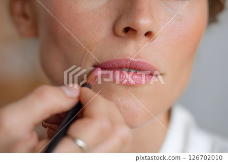 Beautiful close-up of a woman's mouth being applied with lipstick by a makeup artist Beautiful close-up of a woman's mouth being applied with lipstick by a makeup artist 126702010