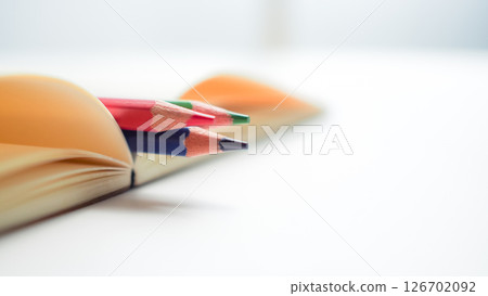 Close-up of colored pencils placed inside the fold of an open notebook, with shallow depth of field and soft light. Represents creativity, inspiration, and back-to-school themes. 126702092