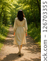 Back view of a woman walking through the sunlight filtering through the trees 126703355