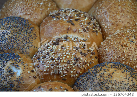 Close-up of assorted rolls featuring sesame seeds, poppy seeds, and other grains offering a variety of textures and flavors. Close-up of assorted rolls featuring sesame seeds, poppy seeds, and other grains offering a variety of textures and flavors. 126704348