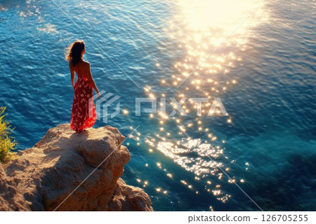 Serene woman on cliff gazes at sparkling ocean during golden hour 126705255