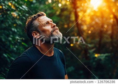 Man with rugged features stands in tranquil forest with sunlight filtering through trees 126706286