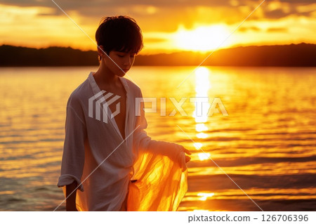 Teenage boy standing by a lake at sunrise in a flowing white shirt glowing in the sunlight 126706396