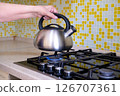 A woman's hand places a kettle of water on a gas stove. Home cooking 126707361