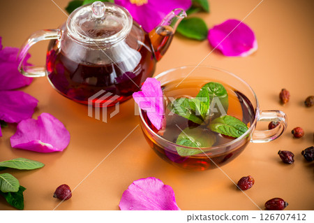 Healing tea with rosehip and mint in transparent cup and teapot on brown background Healing tea with rosehip and mint in transparent cup and teapot on brown background 126707412