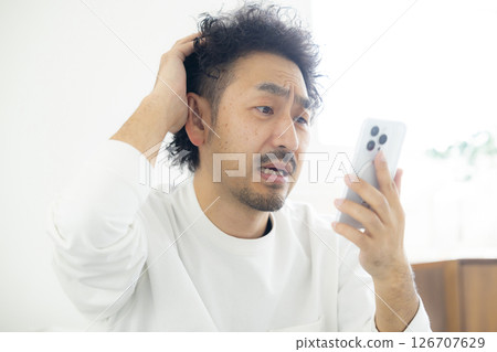 A man holding his head while looking at his smartphone 126707629