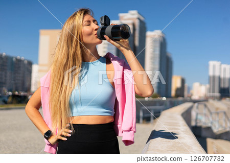 Sport woman jogger runner drinking water from bottle at city embankment river closeup 126707782