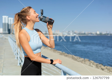 Sport woman jogger runner drinking water from bottle at city embankment river closeup 126707799