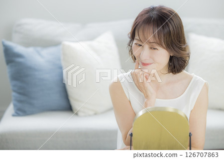 Middle-aged woman looking in the mirror in the living room 126707863