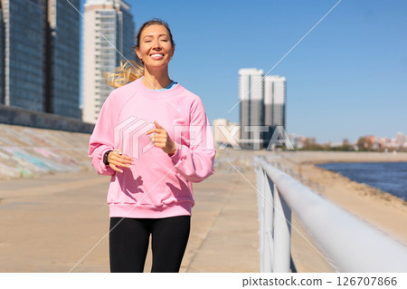 Portrait smiling woman jogging running at sunny city embankment healthy lifestyle Portrait smiling woman jogging running at sunny city embankment healthy lifestyle 126707866