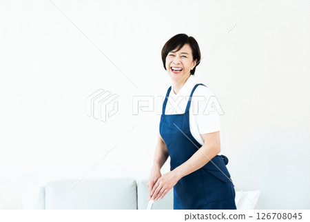 A woman in an apron cleaning the living room 126708045