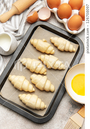 Baking tray with raw croissants, waiting to be cooked, surrounded by kitchen utensils Baking tray with raw croissants, waiting to be cooked, surrounded by kitchen utensils 126708097