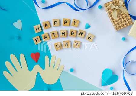 Fathers Day photo with paper hands shirt mustache tie gift box Happy Fathers Day wooden letters blue red hearts festive flat lay top view white and blue background for dad 126709708