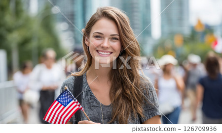 A young happy American woman walks through a city where there are many other people, with a small American flag in her hands, the background is blurred. Election Day in the USA. America Day. Festive 126709936