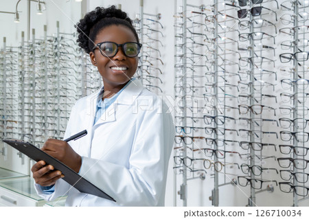 Female optician in lab coat making notes and smiling 126710034