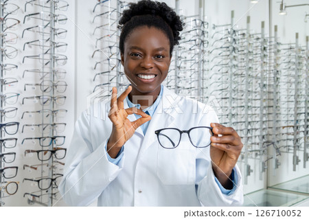Smiling dark-skinned optician presenting new model of eyeglasses 126710052