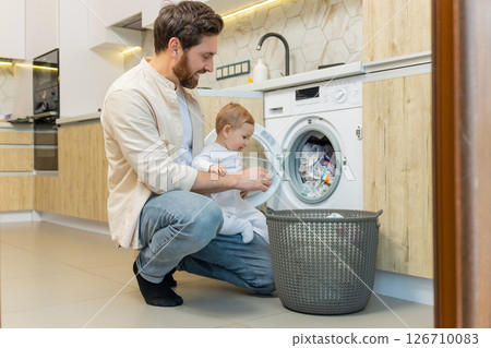 Young man and his little son sorting clothes before putting into washing machine Young man and his little son sorting clothes before putting into washing machine 126710083