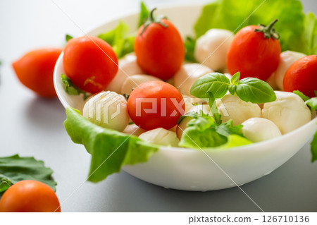 mini mozzarella in white bowl with herbs and cherry tomatoes on grey background mini mozzarella in white bowl with herbs and cherry tomatoes on grey background 126710136