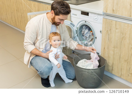 Young man and his little son sorting clothes before putting into washing machine 126710149