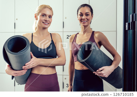 Women in sportswear with the rolled yoga mats looking excited Women in sportswear with the rolled yoga mats looking excited 126710185