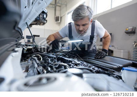 Mechanic examining engine components with flashlight Mechanic examining engine components with flashlight 126710218